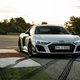 a grey 2023 audi r8 gt parked on the red and white striped curbing of a race track with the sun setting in the background